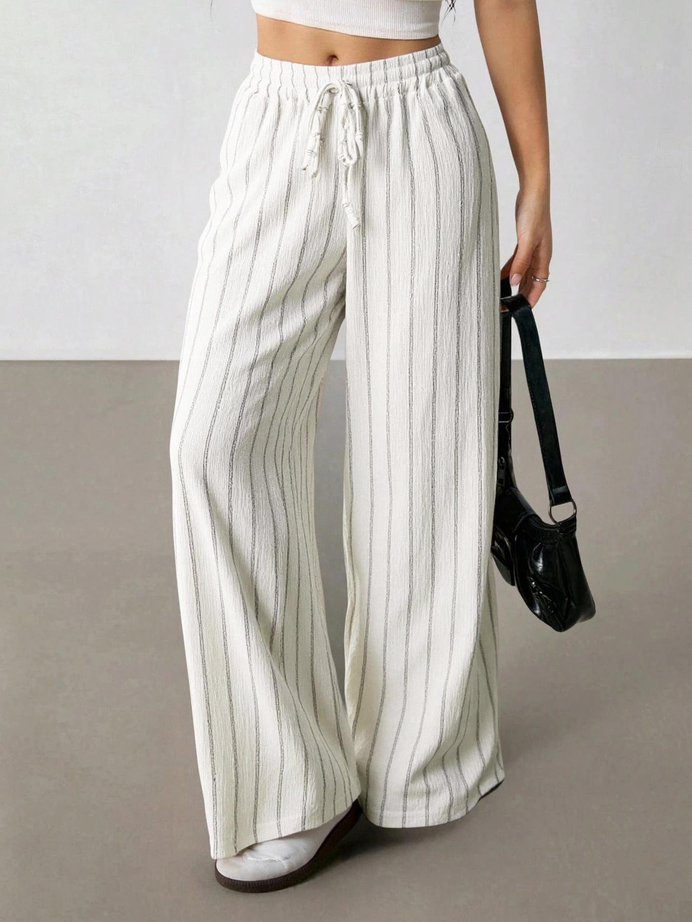 Off White Striped Wide Leg Pants Casual Vacation Daily Outfit Lifestyle shot cream white vertical striped palazzo pants, elastic drawstring waist, crinkle texture, match white crop top and black shoulder bag minimalist indoor backdrop
