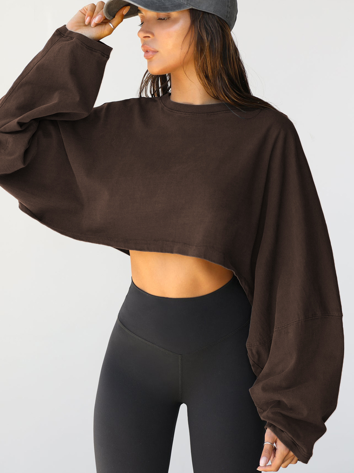 Brown Oversized Cropped Long Sleeve Sweatshirt - Front Angle View Womens brown oversized cropped long sleeve sweatshirt, vintage pigment dyed finish, loose fit with dropped shoulders, paired with black high-waisted leggings, front angle view