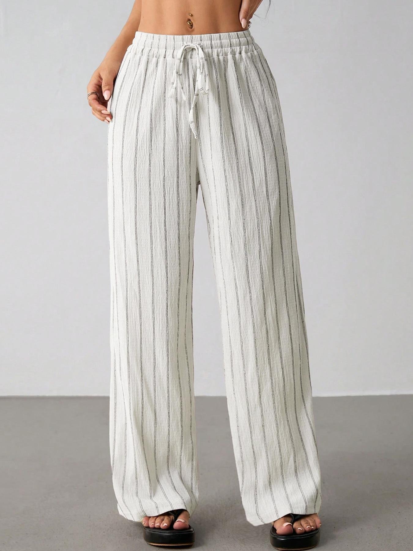 Off White Striped Wide Leg Pants Loose Floor Length Palazzo Trousers Full front shot cream white vertical striped wide leg trousers, elastic drawstring waist, crinkle wrinkle fabric, match white crop top and black slide sandals neutral gray floor background