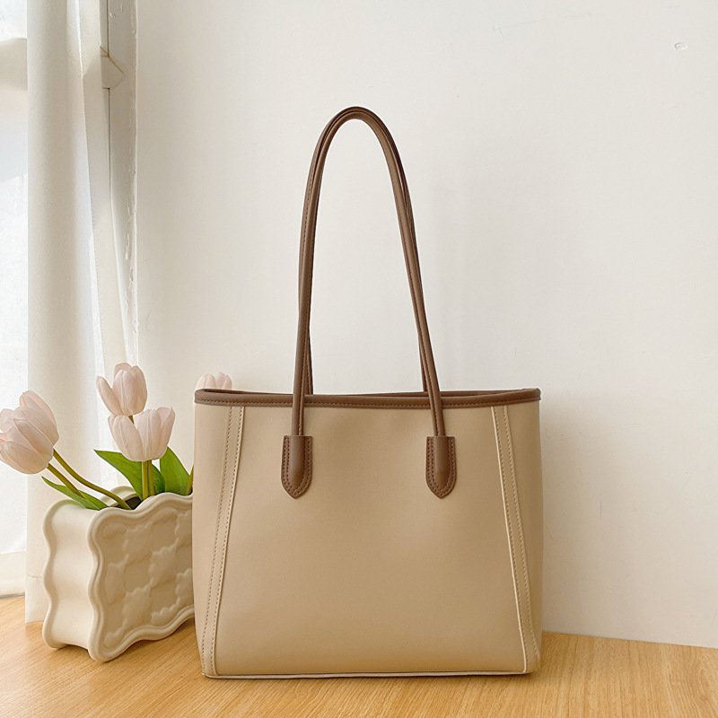 Cream beige women daily tote bag, two-tone brown edge trim, soft faux leather upright structure, long shoulder handles placed beside tulip vase minimalist wood table background