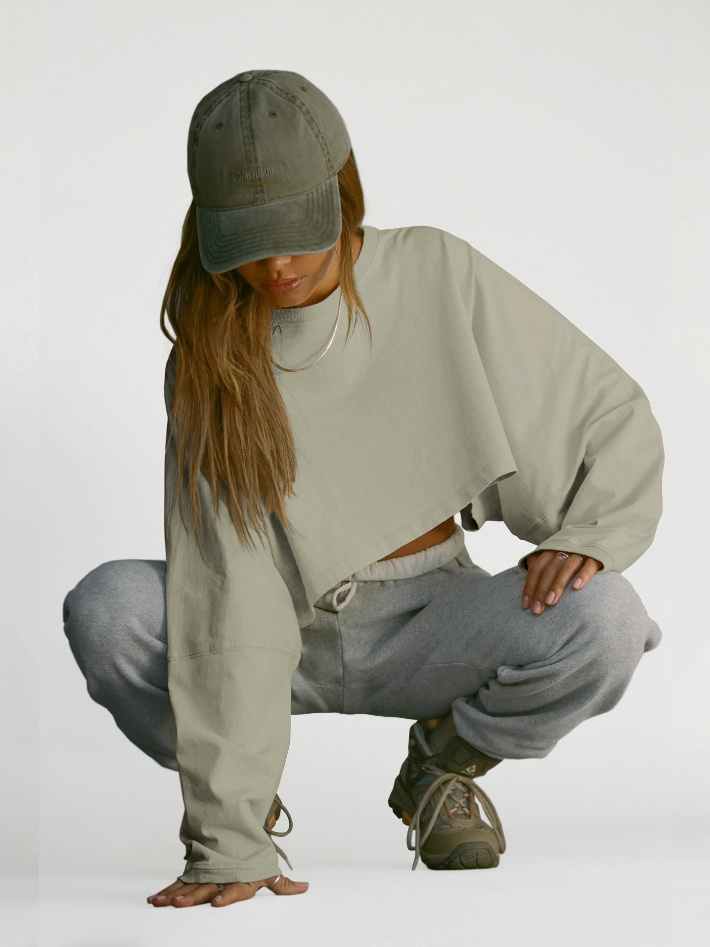 Light Green Cropped Sweatshirt - Casual Streetwear View Womens light green cropped oversized sweatshirt, long sleeve balloon fit, vintage wash fabric, casual streetwear style, squat pose with grey sweatpants and sneakers
